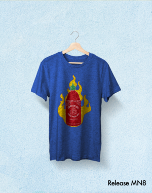​​A blue t-shirt with a red Sriracha bottle on fire that says, “Turn up the heat. Abolish ICE. Free Them All.” The t-shirt is on a hanger.