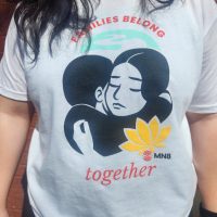 A white t-shirt with a child and a caretaker hugging that says, "Families Belong Together." Design created by Brenda Tran.